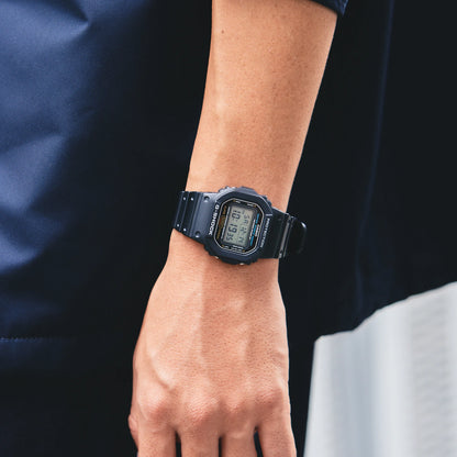 Reloj Casio G-Shock DW-5600 digital negro en la muñeca de una persona con ropa azul.