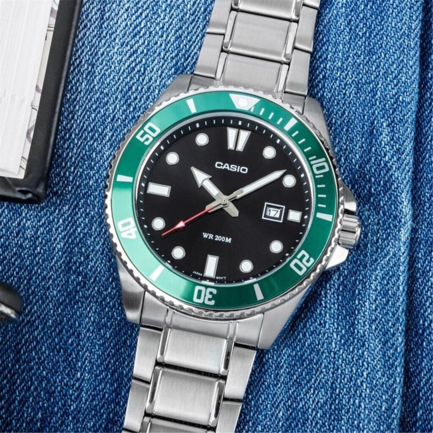 Casio MDV-107D-3A stainless steel dive watch with black dial, green unidirectional bezel and stainless steel bracelet displayed in casual lifestyle setting.