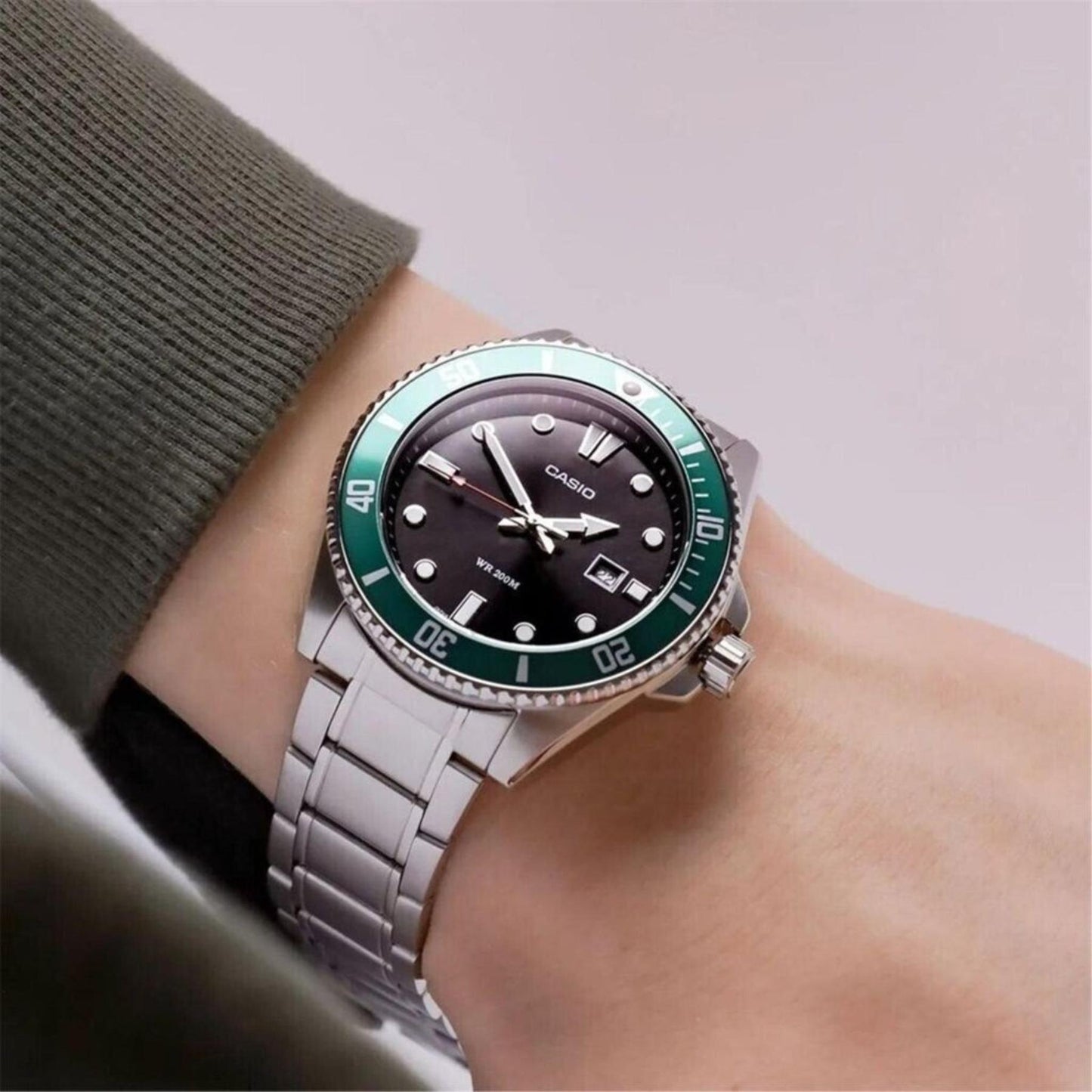 Casio MDV-107D-3A stainless steel dive watch worn on wrist with black dial, green unidirectional bezel and stainless steel bracelet.