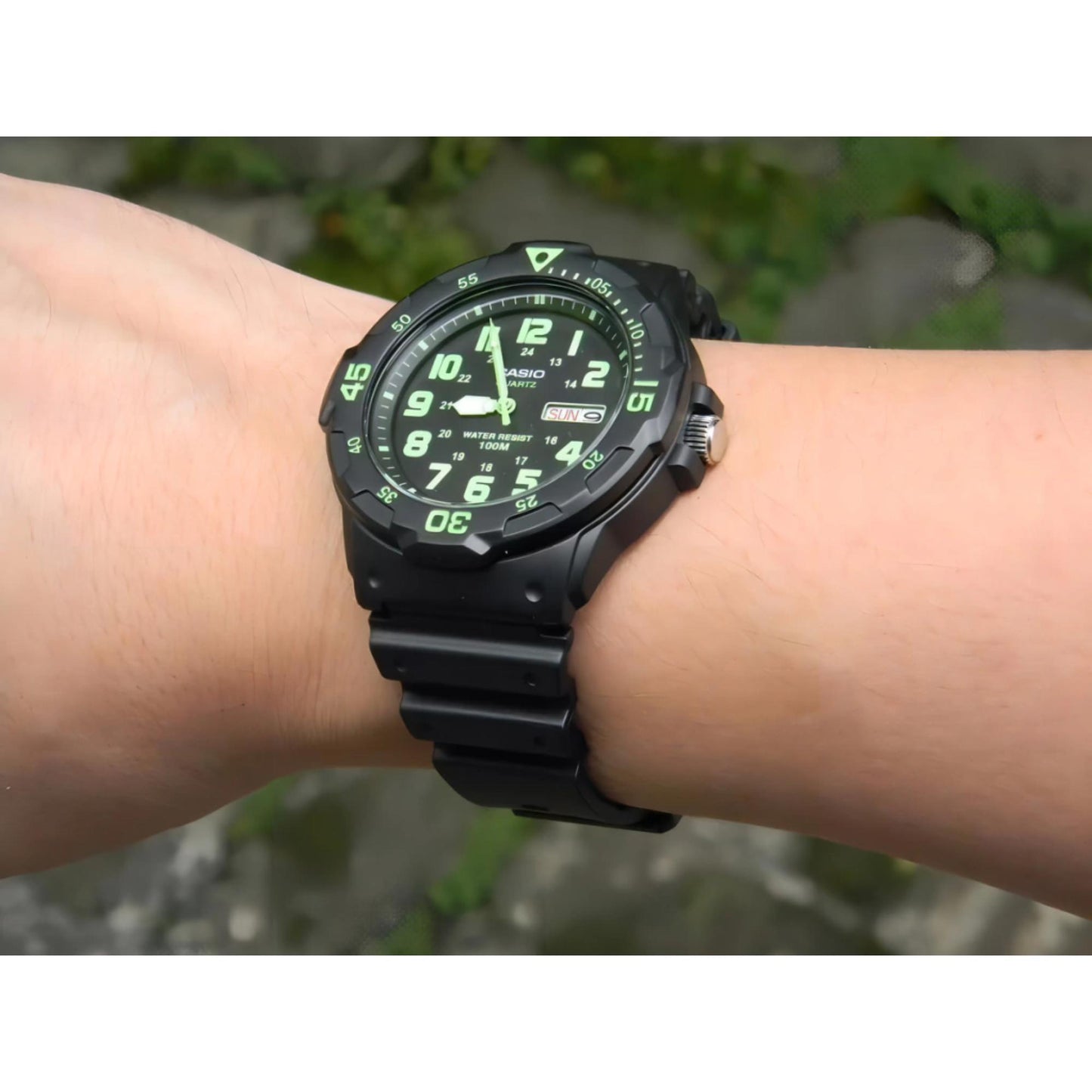 Casio MRW200H-3BV dive style sport watch worn on wrist outdoors with black dial, green numerals, rotating bezel and black resin strap.