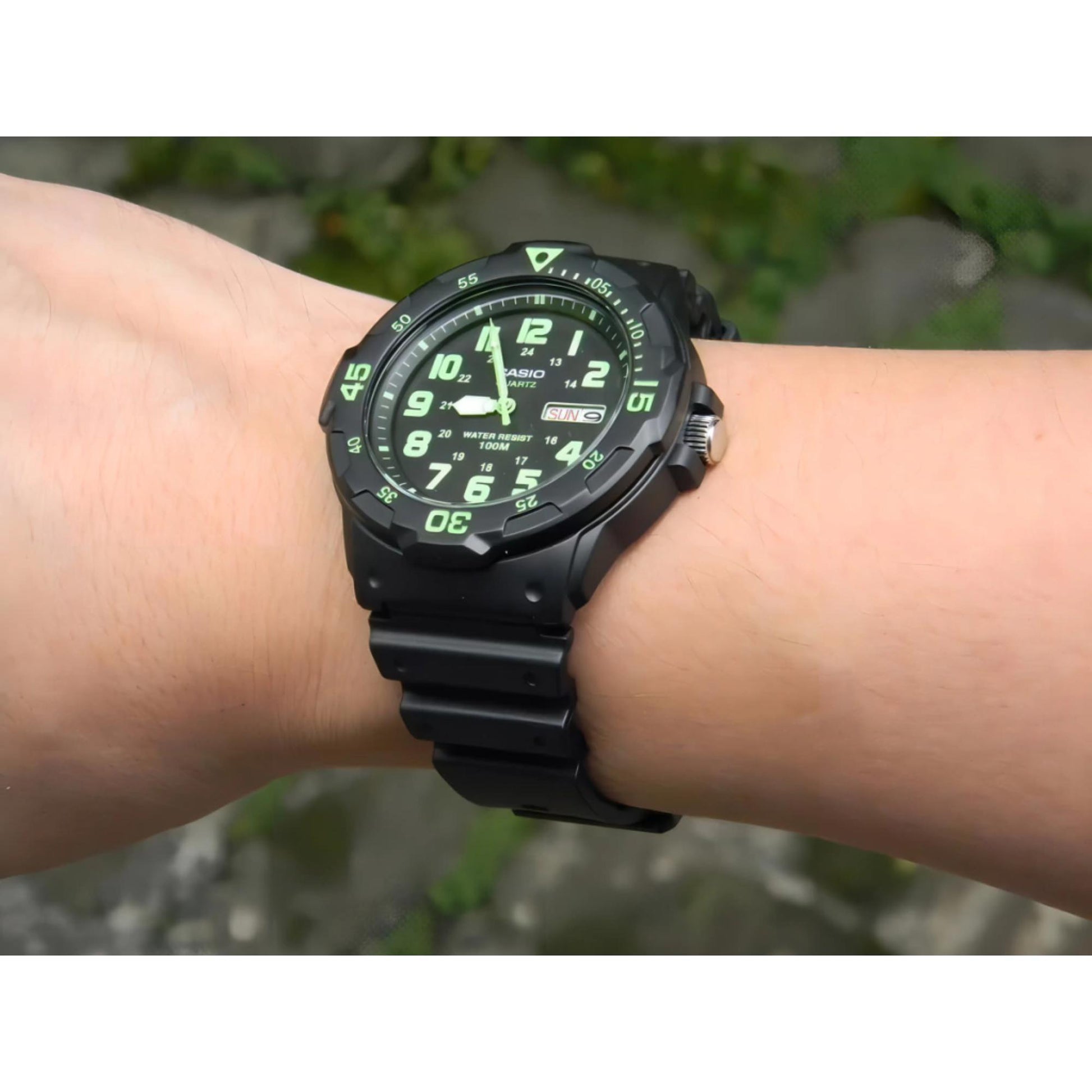 Casio MRW200H-3BV dive style sport watch worn on wrist outdoors with black dial, green numerals, rotating bezel and black resin strap.