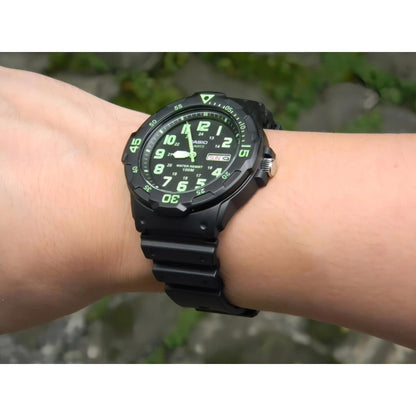Casio MRW200H-3BV dive style sport watch worn on wrist outdoors with black dial, green numerals, rotating bezel and black resin strap.
