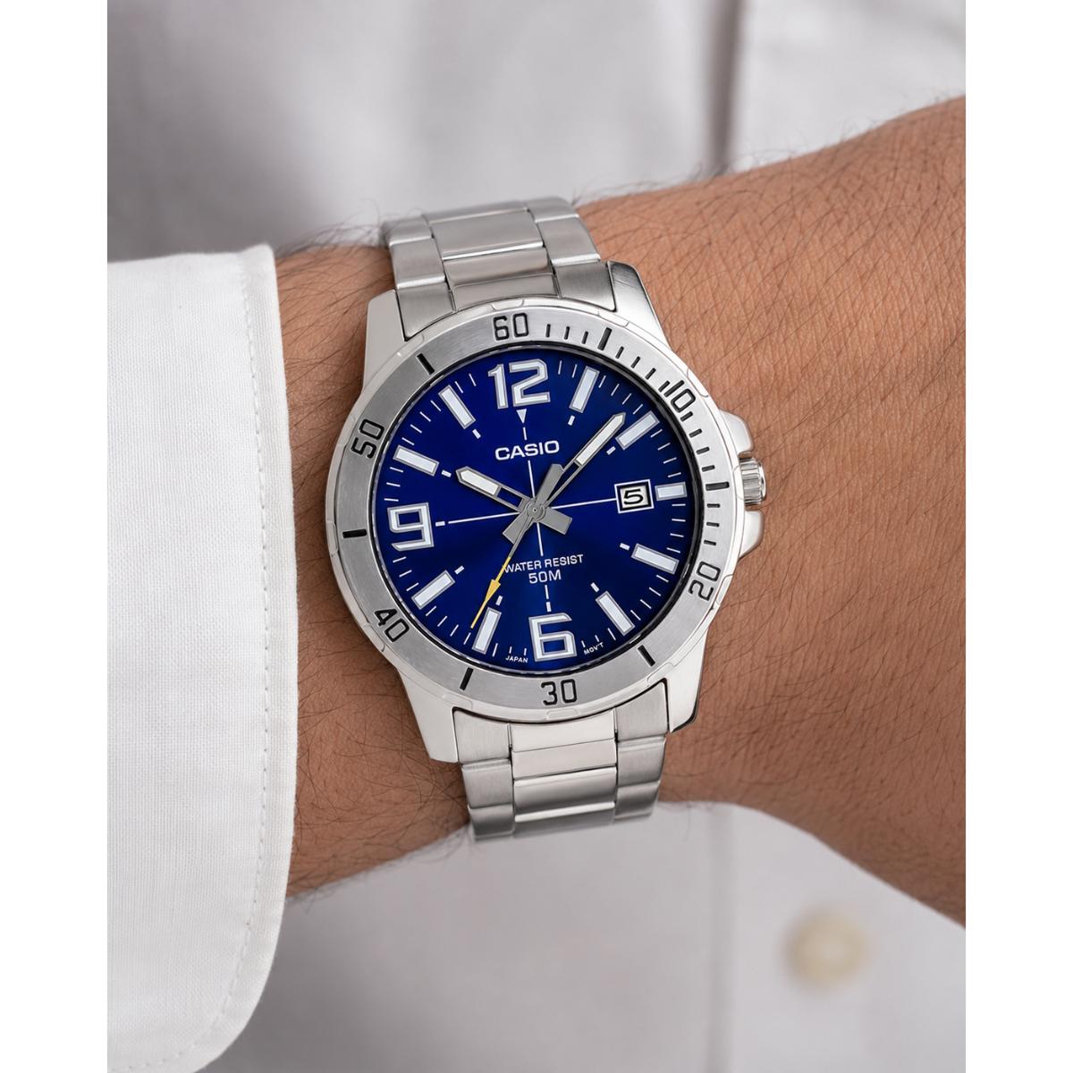 Man wearing the Casio MTP-VD01D-2BV stainless steel watch featuring a vibrant blue dial, silver-tone diver-style bezel, luminous hands and hour markers, date display, and stainless steel bracelet in an everyday lifestyle setting.