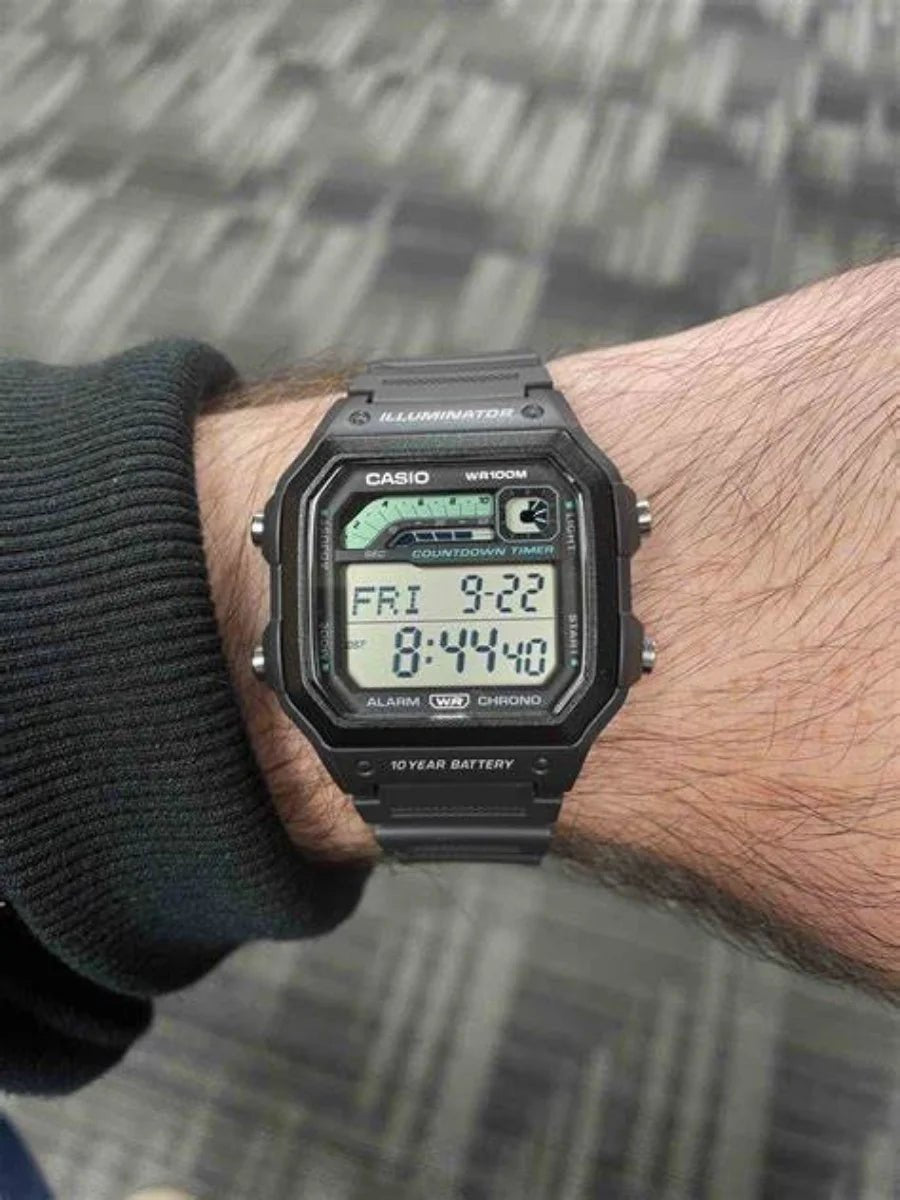 Reloj Casio digital negro en muñeca de hombre, correa de resina y pantalla rectangular.