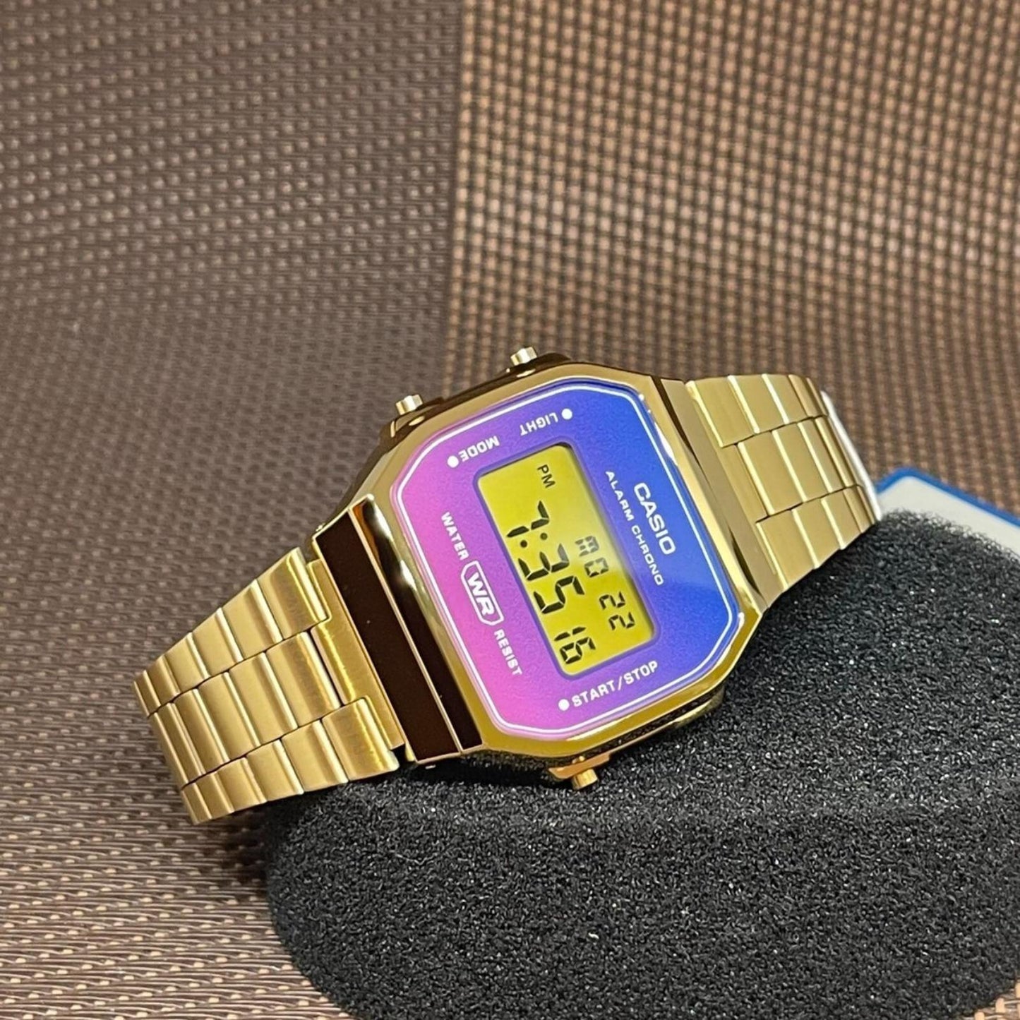 Casio Vintage A168WERG-2ADF with a blue, purple, and pink gradient digital display, gold-tone case, side push buttons, and matching bracelet.