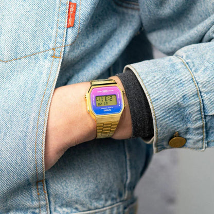 Casio Vintage A168WERG-2ADF worn on the wrist with a blue, purple, and pink gradient digital display, gold-tone case, and matching bracelet.