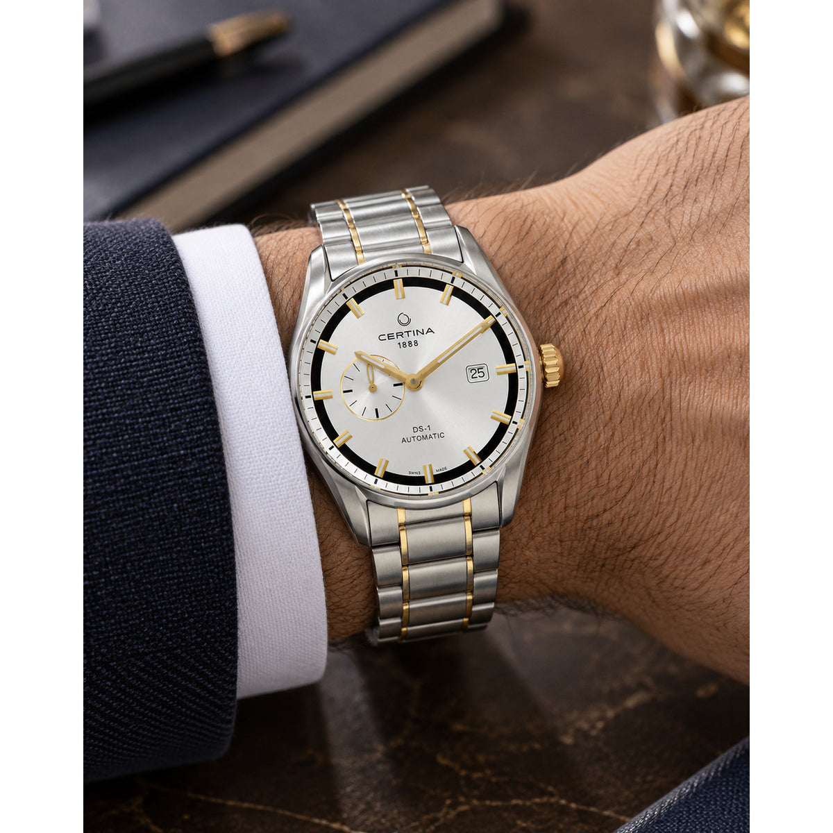 Certina DS-1 automatic men's watch worn on the wrist featuring a silver dial, gold-tone accents, and a two-tone stainless steel bracelet.
