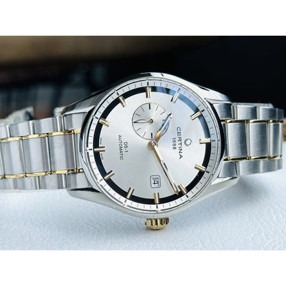 Certina DS-1 automatic men's watch angled to highlight the silver sunburst dial, gold-tone hands, small seconds subdial, and date window.