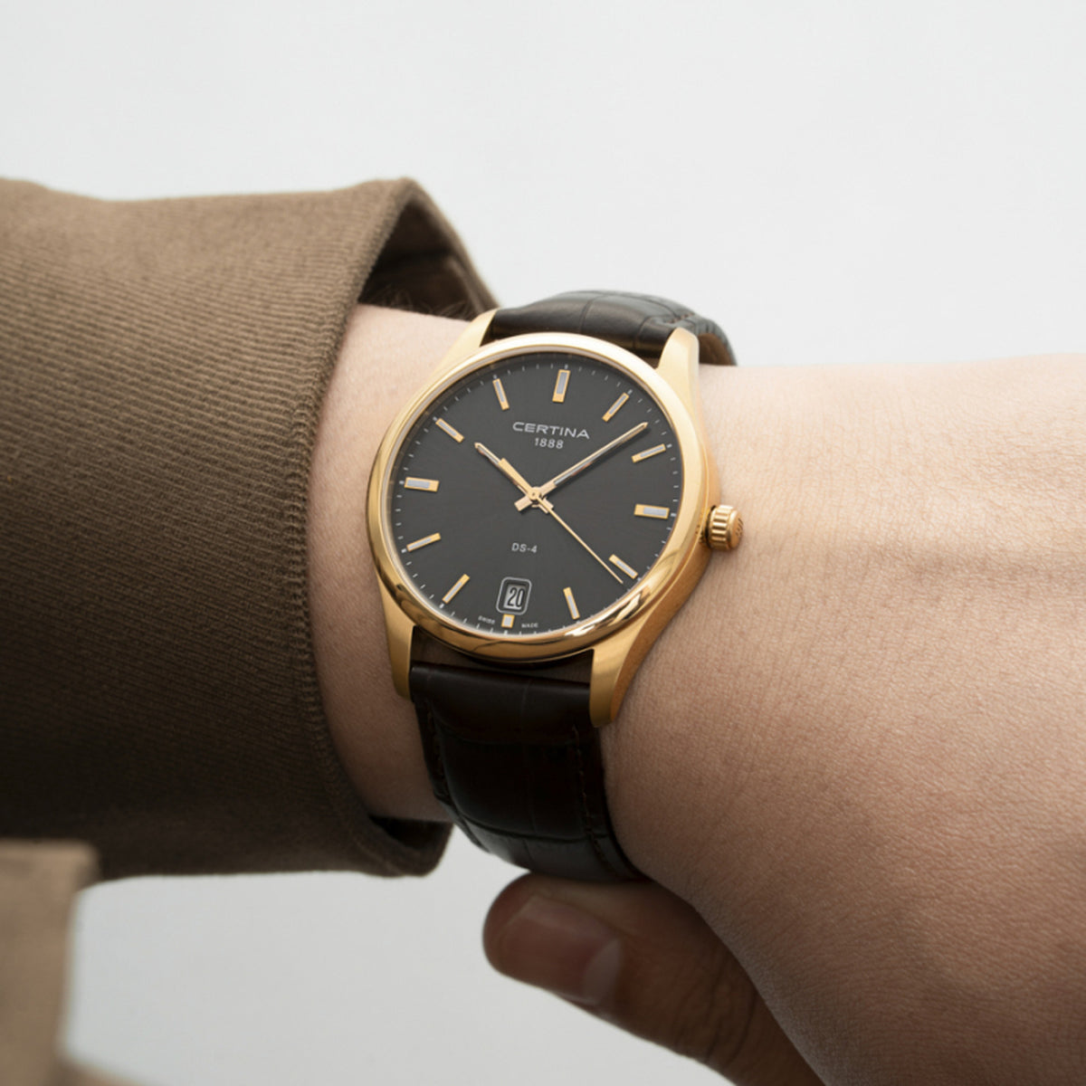 Certina DS-4 C022.610.36.081.00 men's quartz watch worn on wrist with a gold-tone stainless steel case, gray dial, and dark brown leather strap