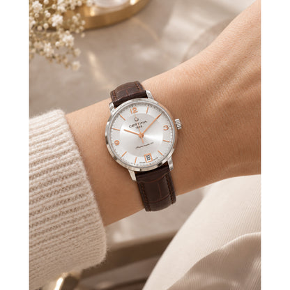 Certina DS Caimano women's automatic watch worn on wrist with a silver dial, rose gold-tone markers, and a brown leather strap