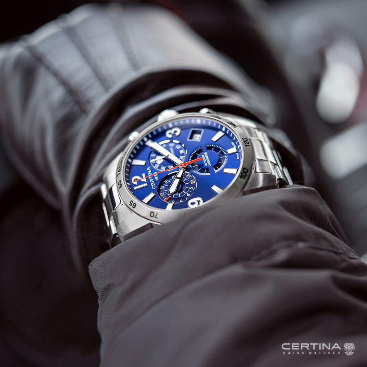 Certina DS Podium C034.654.11.047.00 with a blue chronograph dial, red accents, silver-tone tachymeter bezel, and matching bracelet worn on the wrist.