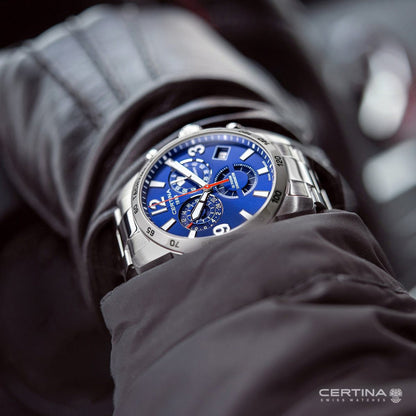 Certina DS Podium C034.654.11.047.00 with a blue chronograph dial, red accents, silver-tone tachymeter bezel, and matching bracelet worn on the wrist.