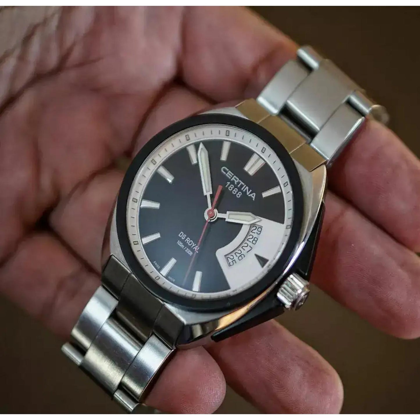 Reloj Certina DS Royal C010.410.11.051.00 sostenido en la mano, con esfera negra, indicador de fecha curvado y brazalete de acero inoxidable cepillado.