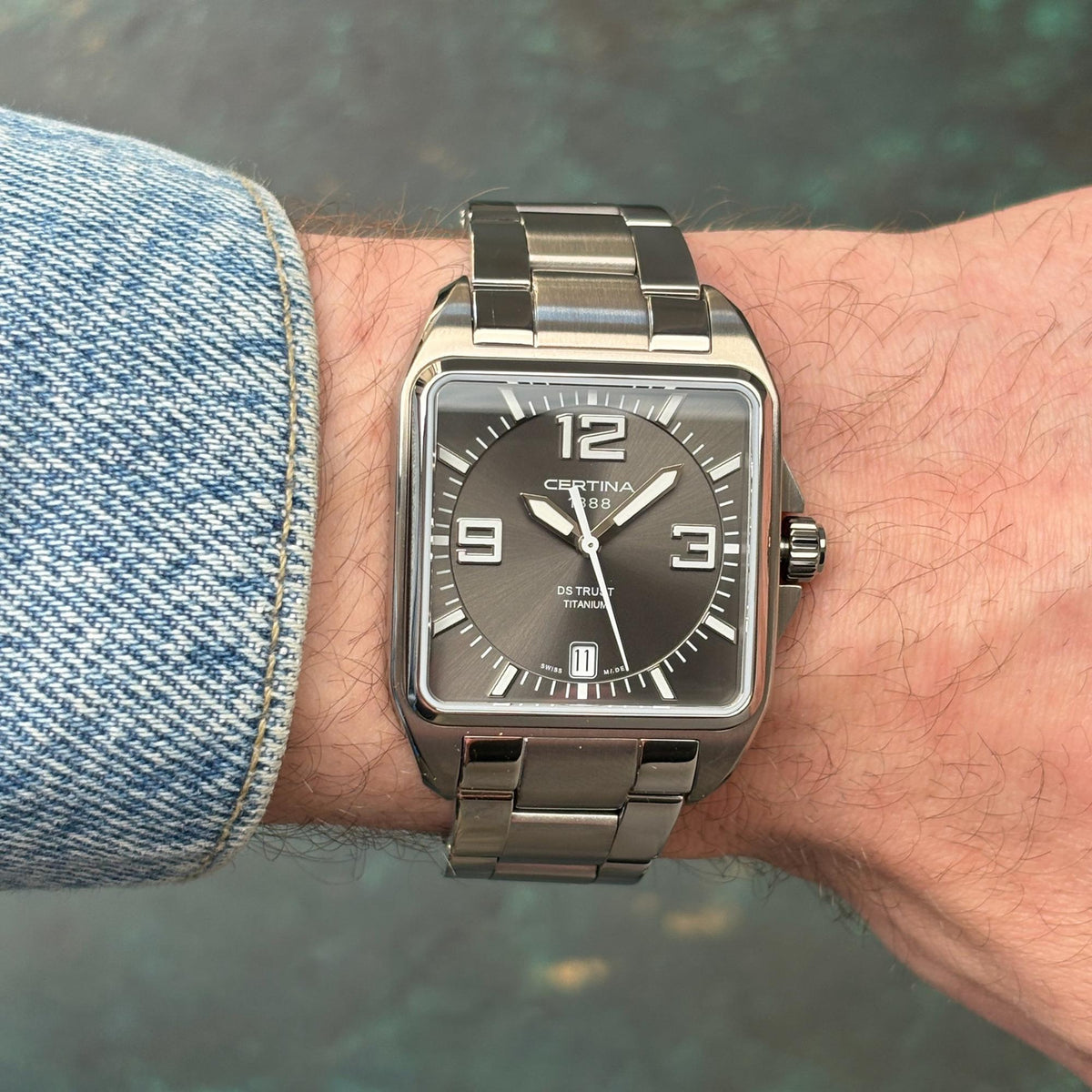 Certina DS Trust C019.510.44.087.00 with a grey dial, bold silver-tone Arabic numerals, square titanium case, date window, and matching titanium bracelet worn on the wrist.