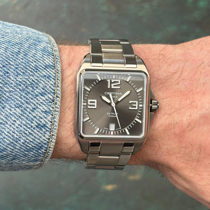 Certina DS Trust C019.510.44.087.00 with a grey dial, bold silver-tone Arabic numerals, square titanium case, date window, and matching titanium bracelet worn on the wrist.