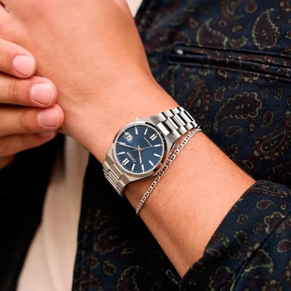 Reloj Citizen automático de acero con esfera azul lucido en la muñeca junto a una pulsera metálica, estilo elegante.