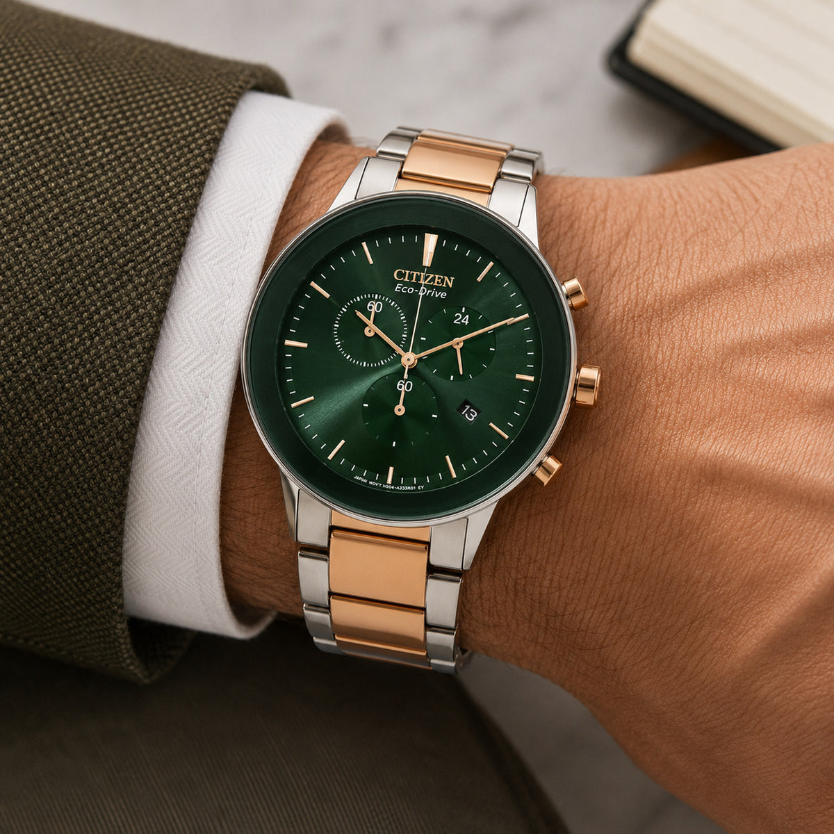 Citizen Axiom AT2244-84X with a green chronograph dial, rose gold-tone accents, and a two-tone stainless steel bracelet worn on the wrist.