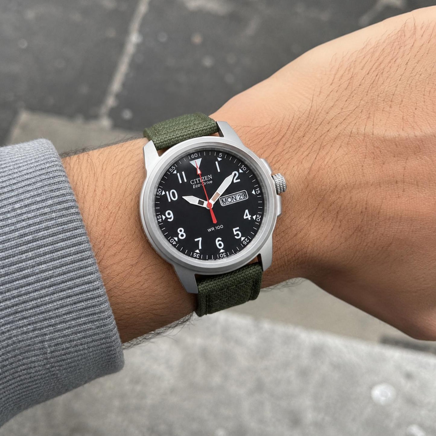 Citizen BM8180-03E worn on the wrist with black dial, white Arabic numerals, day-date display, stainless steel case, and green nylon strap.