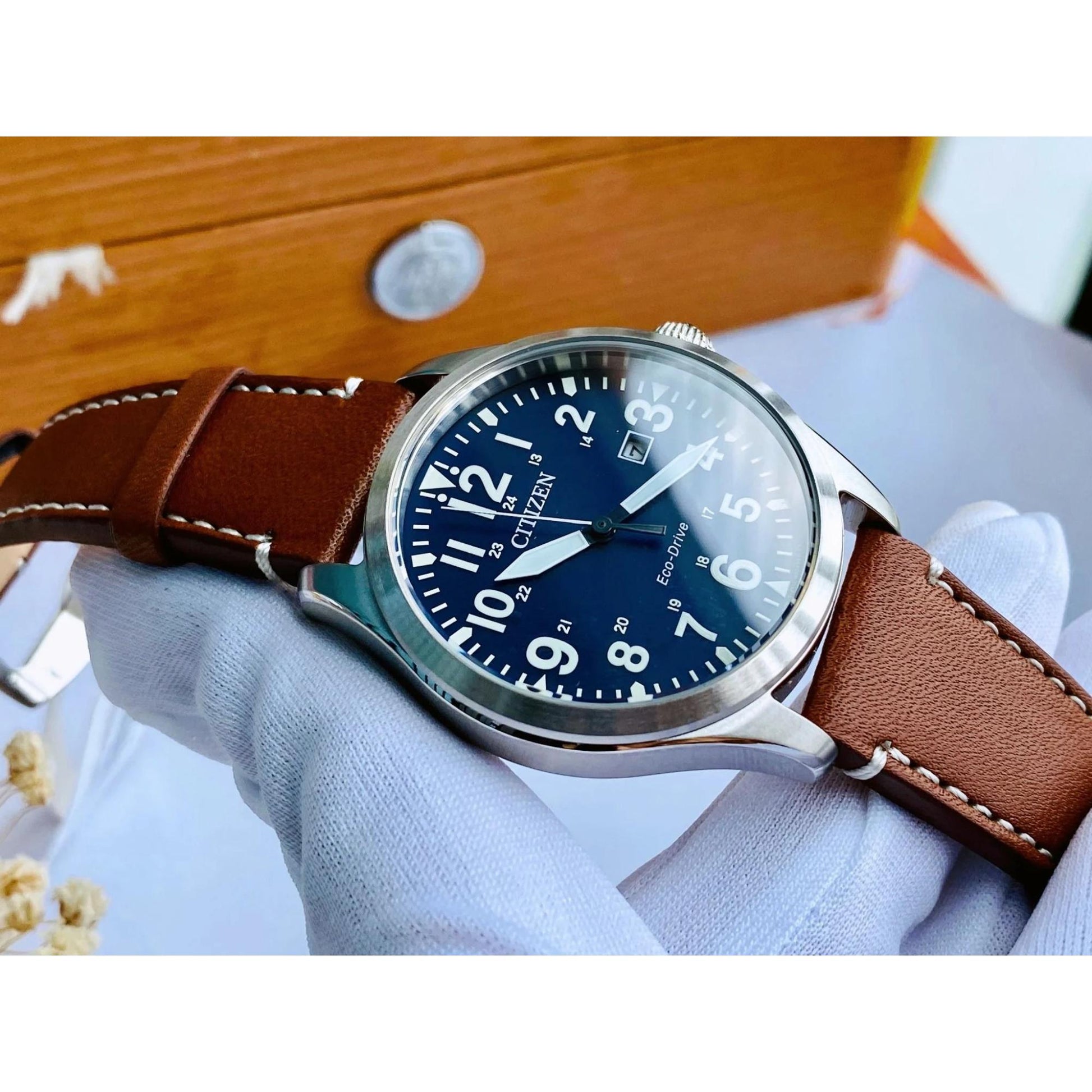 Citizen Eco Drive field watch with blue dial and brown leather strap held in hand showing stainless steel case and classic military style