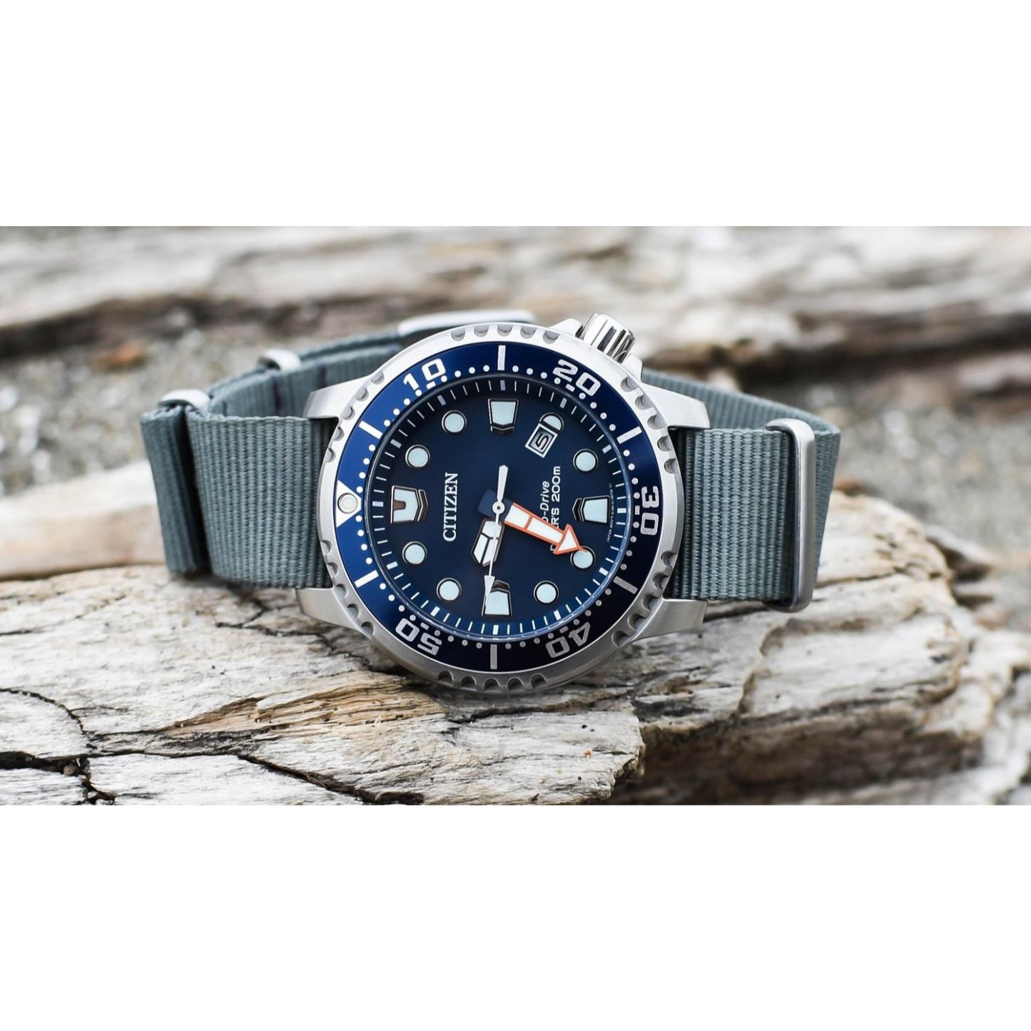 Citizen Eco-Drive Promaster Diver BN0151-09L with blue dial, blue rotating bezel, luminous hour markers, date window, stainless steel case, and gray fabric strap resting on a weathered wood surface.