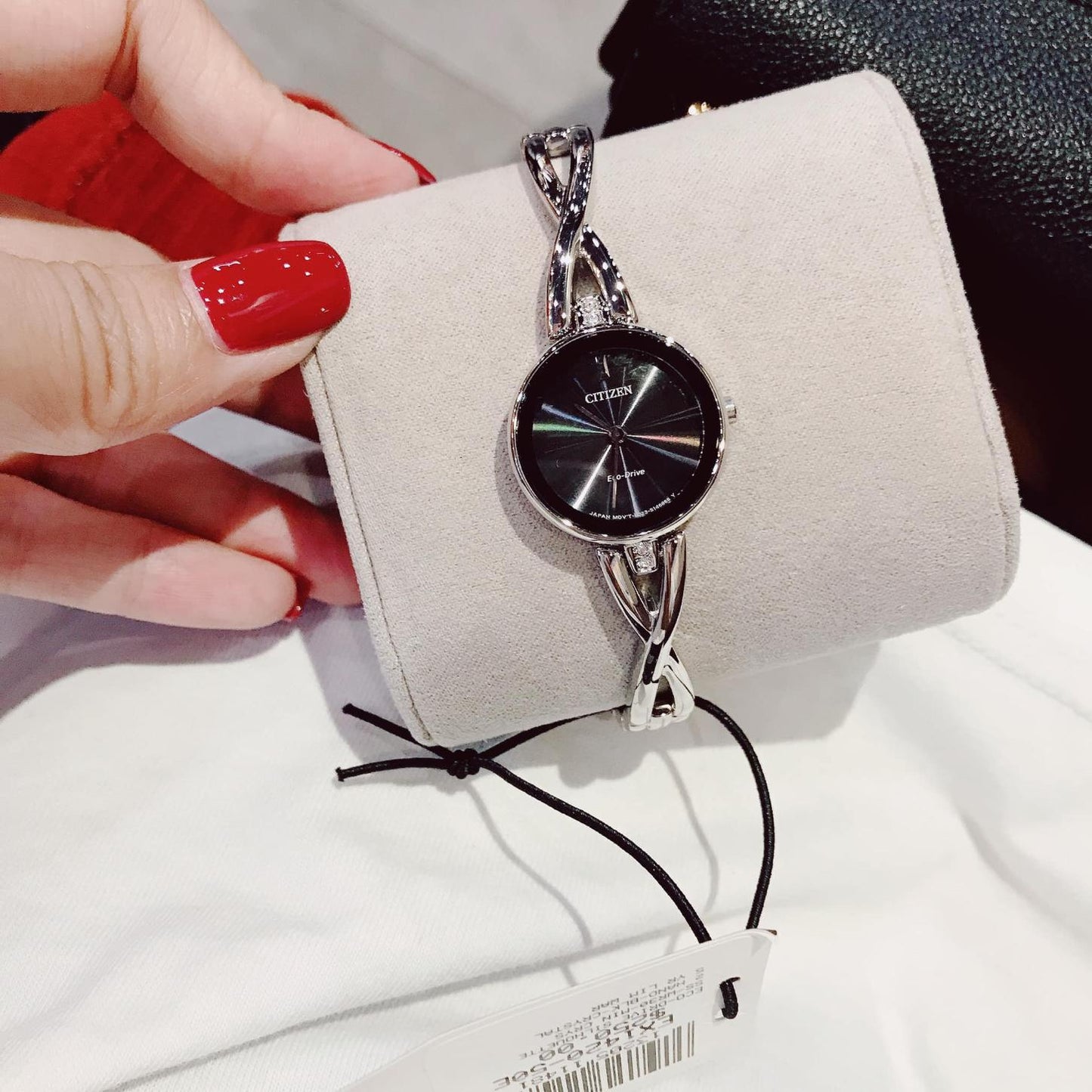 Citizen EX1420-50E Eco-Drive watch with black dial and polished stainless steel bangle bracelet placed on display cushion with twisted design links