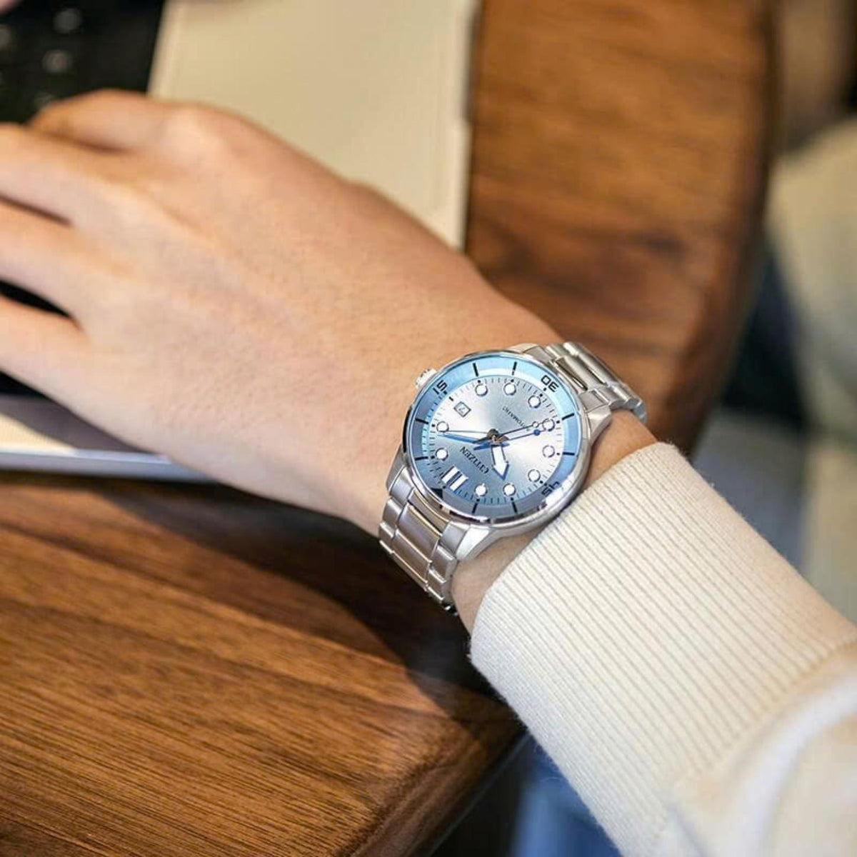Citizen NJ0191-83L automatic timepiece featuring a light blue dial and steel bracelet on a wrist near a laptop.