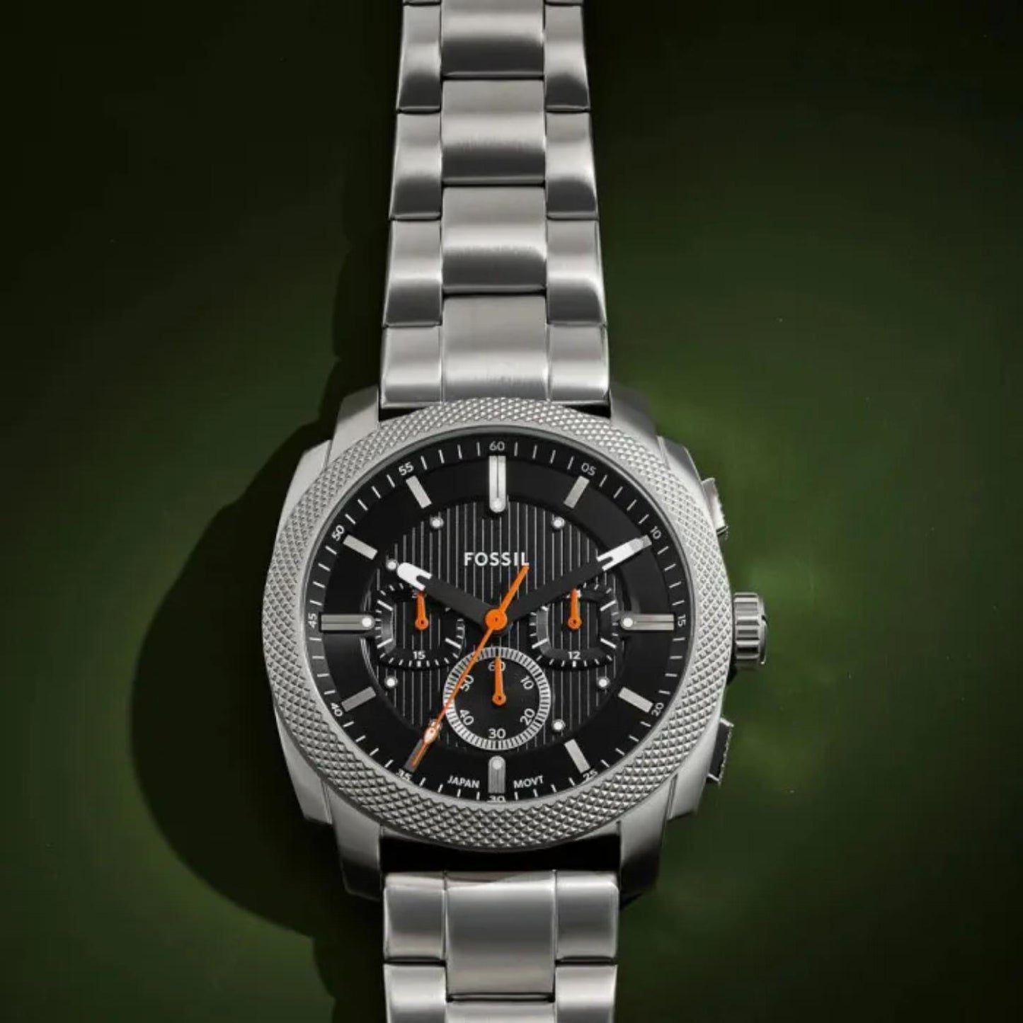Fossil Machine FS6095 chronograph watch with textured black dial, orange accents, knurled stainless steel bezel, and brushed stainless steel bracelet shown in a dramatic close-up view.