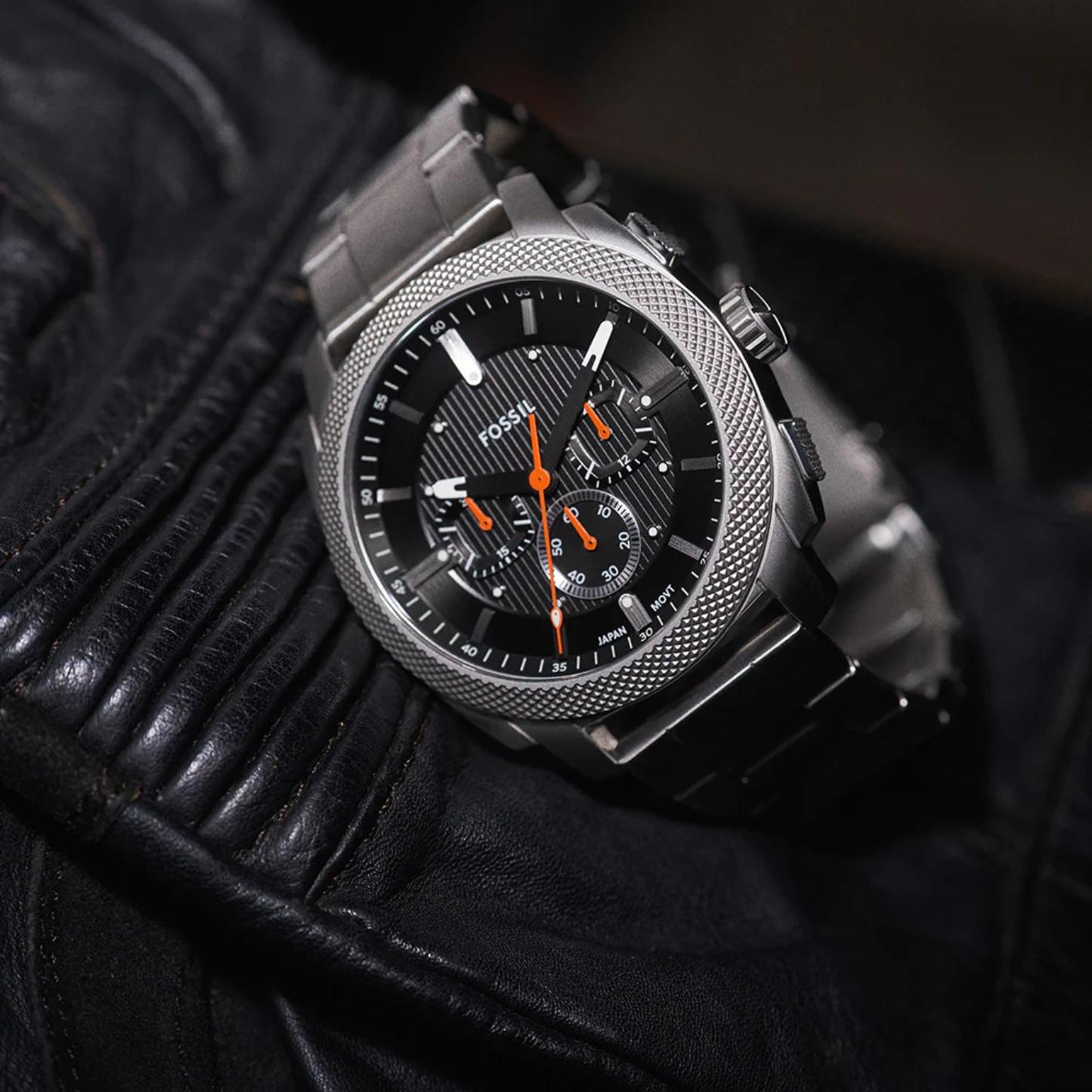 Fossil Machine FS6095 stainless steel chronograph watch with black textured dial and orange accents shown in a rugged lifestyle close-up view.