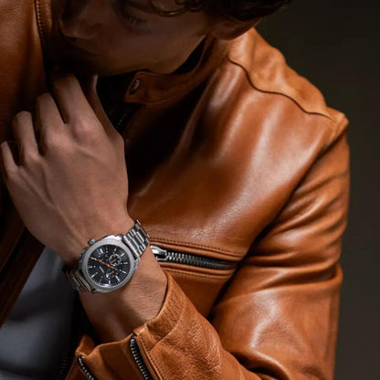 Fossil Machine FS6095 stainless steel chronograph watch with black dial and orange accents worn on the wrist with a brown leather jacket.