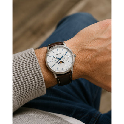 Fossil Neutra FS5905 men’s quartz watch with a silver dial, blue hands and markers, moon phase display, dual subdials, and a dark brown leather strap worn on the wrist.