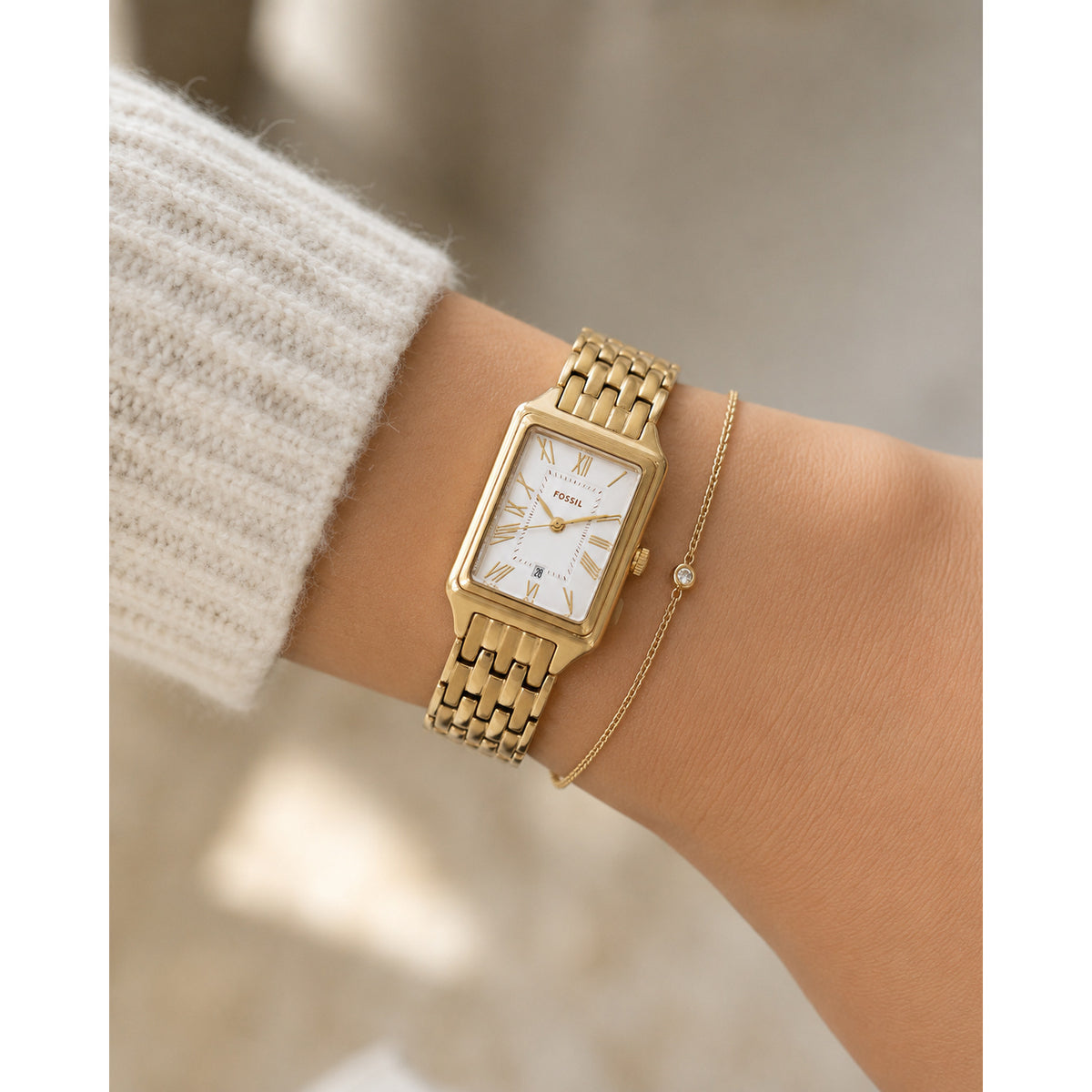 Fossil Raquel ES5220 with a silver dial, gold-tone Roman numeral hour markers, rectangular gold-tone case, date window, and matching gold-tone bracelet worn on the wrist.