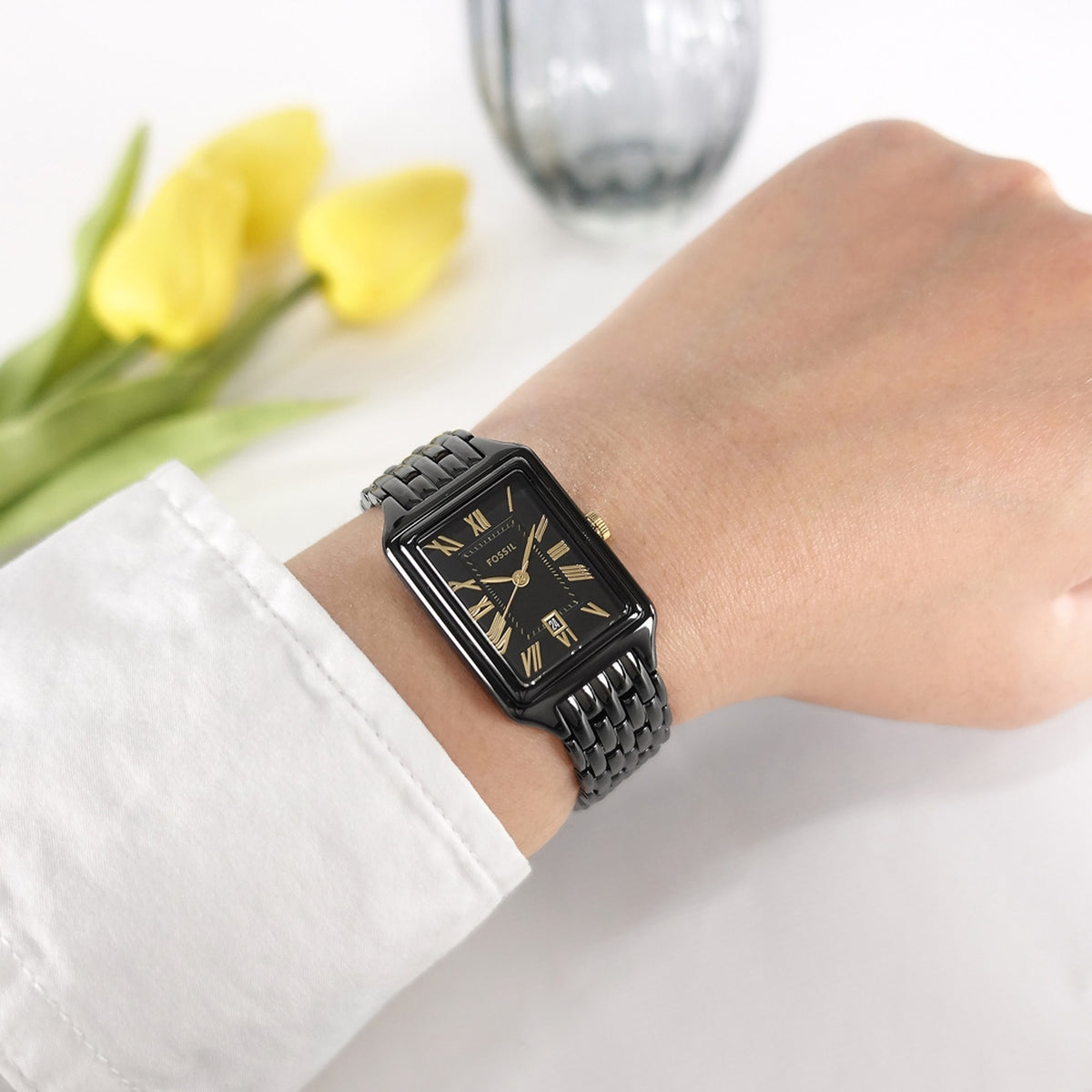 Fossil Raquel ES5385 with a black dial, gold-tone Roman numeral hour markers and hands, rectangular black case, and matching black bracelet worn on the wrist.
