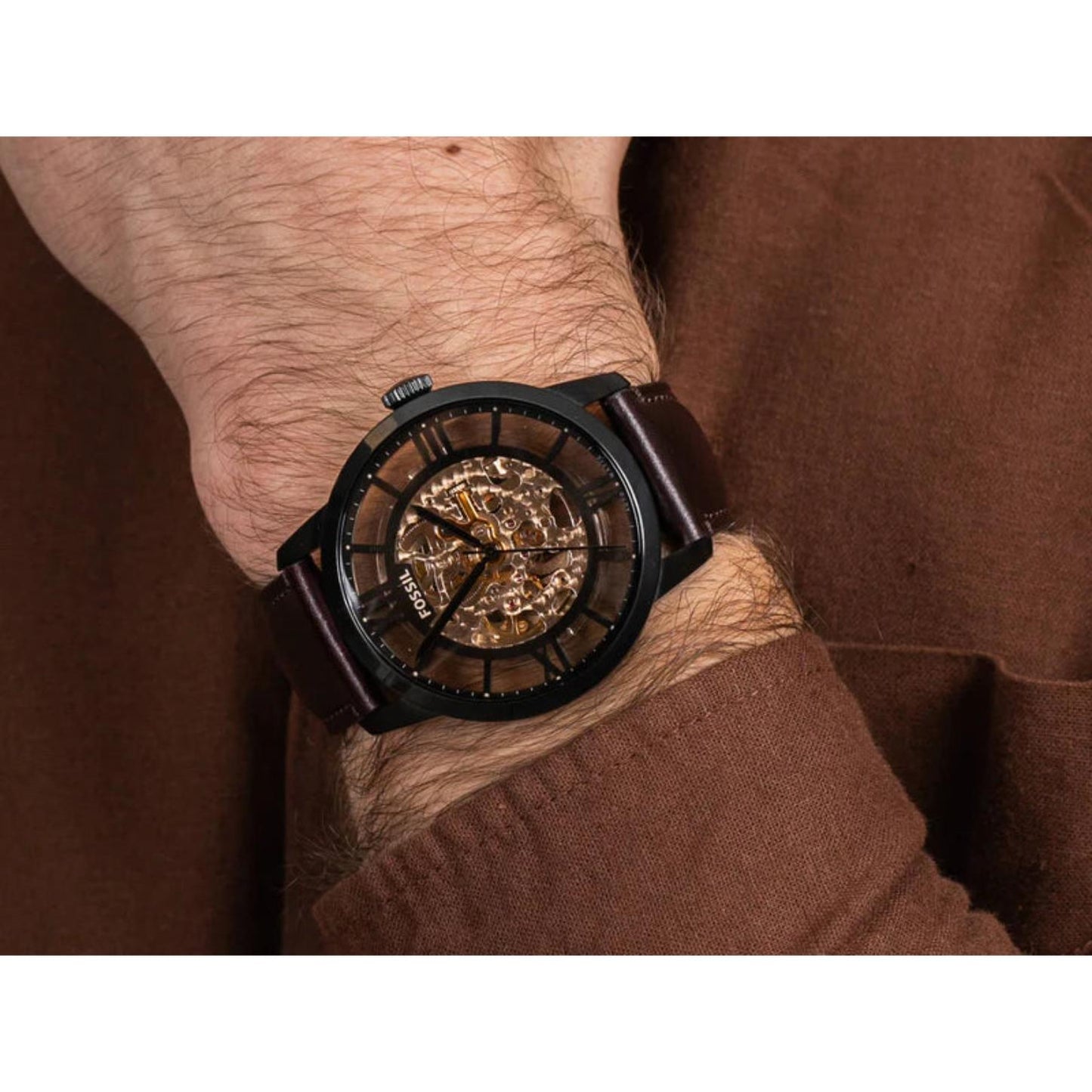 Fossil Townsman ME3098 automatic skeleton watch worn on the wrist, featuring a black stainless steel case, transparent skeleton dial, and brown leather strap in a casual lifestyle setting.