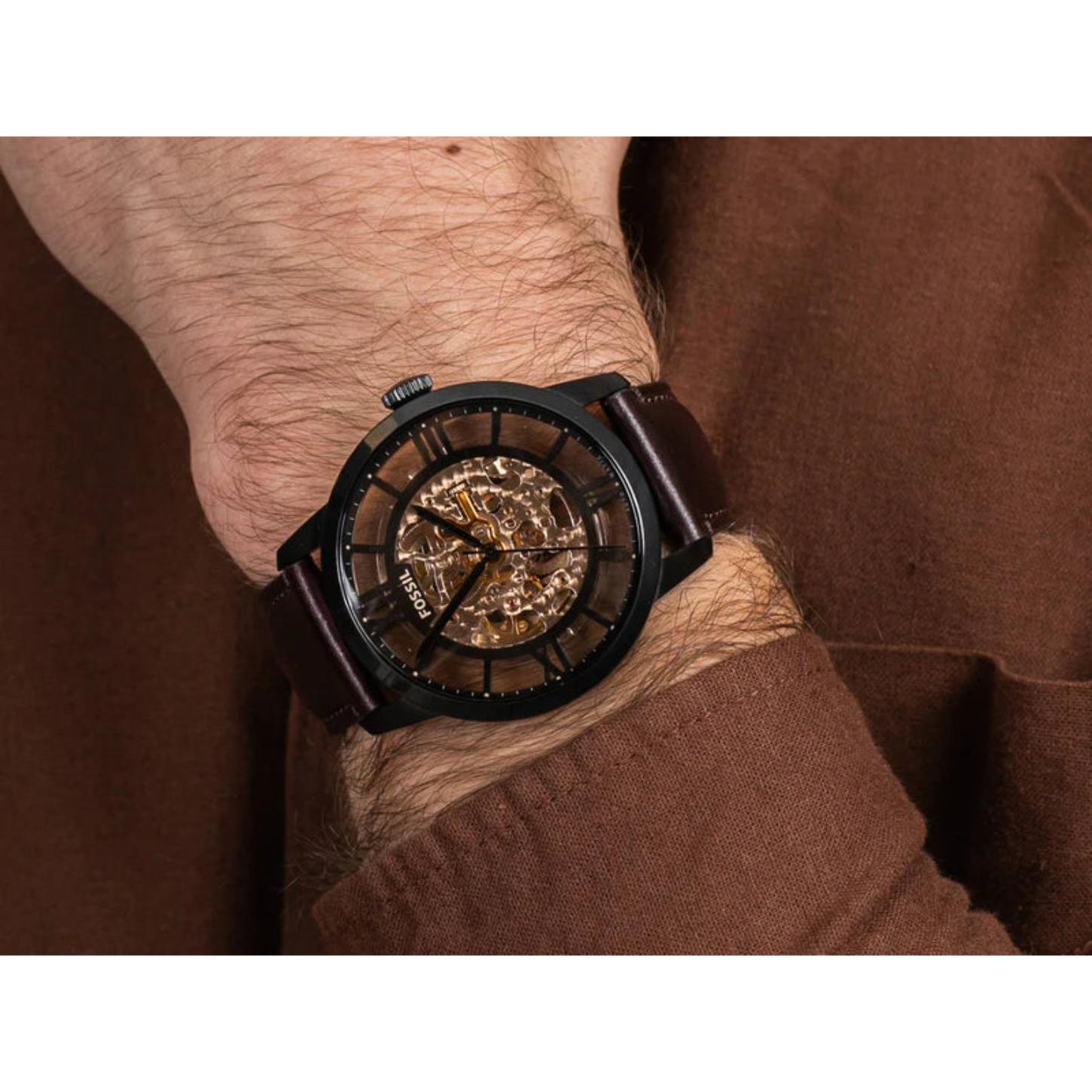 Fossil Townsman ME3098 automatic skeleton watch worn on the wrist, featuring a black stainless steel case, transparent skeleton dial, and brown leather strap in a casual lifestyle setting.
