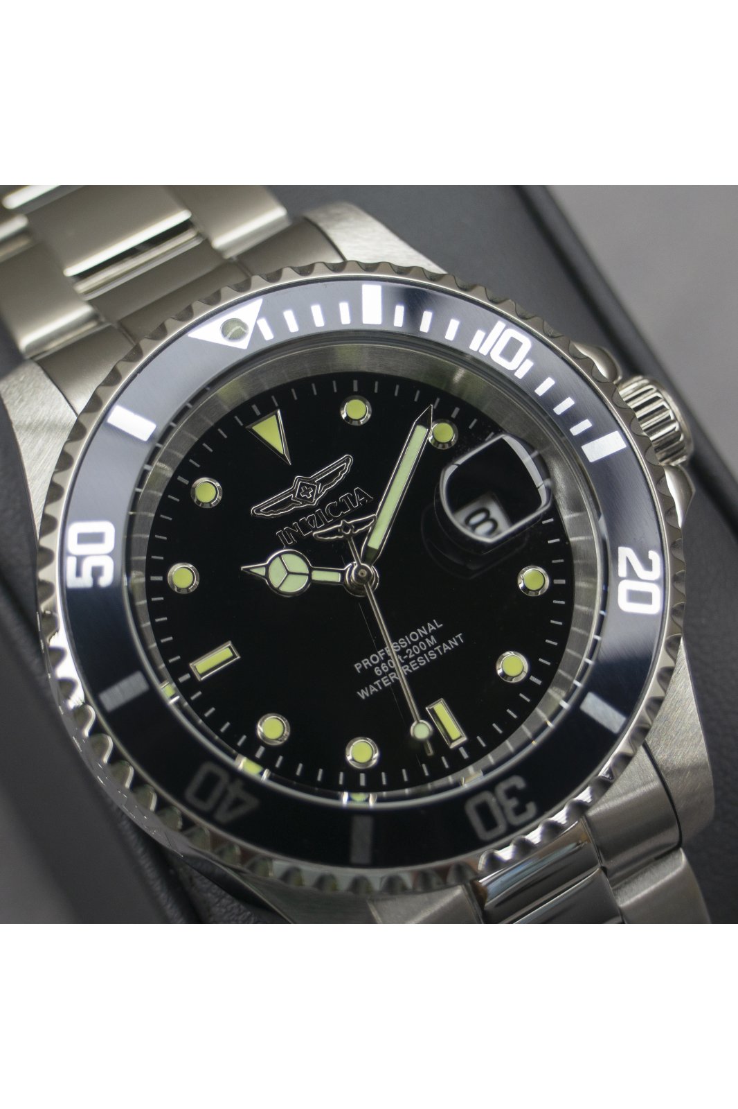 Reloj Invicta analógico de acero con esfera negra y lupa de fecha mostrado en un primer plano detallado.