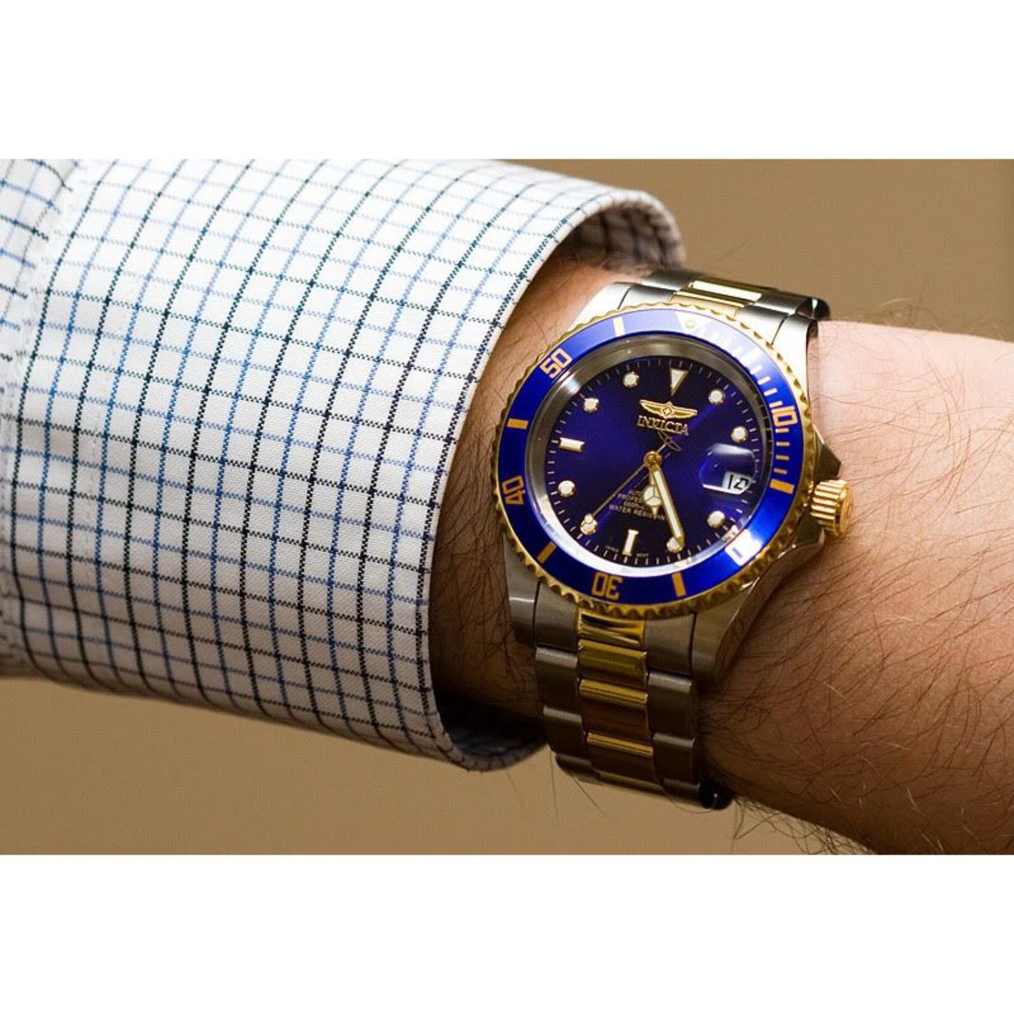 Reloj Invicta Pro Diver 26974 bicolor acero y dorado con esfera y bisel azules, llevado en la muñeca con camisa de vestir a cuadros