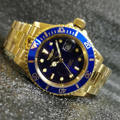 Reloj Invicta Pro Diver 26974 dorado con esfera y bisel azules visto en primer plano en posición inclinada sobre fondo brillante texturizado