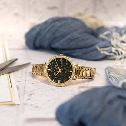 Michael Kors women’s watch with black MK logo dial, crystal bezel and gold-tone stainless steel bracelet placed in lifestyle setting.