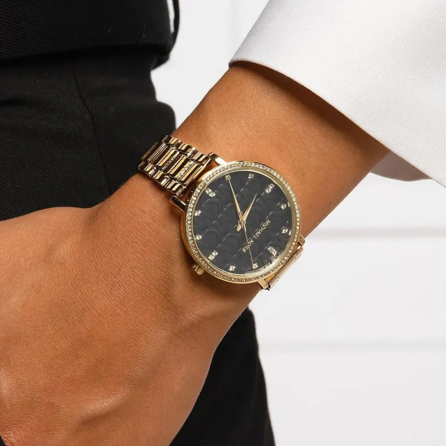 Michael Kors women’s watch worn on wrist with black MK logo dial, crystal bezel and gold-tone stainless steel bracelet.