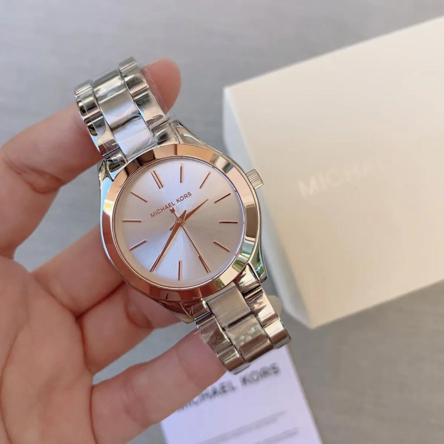 Michael Kors MK3514 Mini Slim Runway women’s watch with white dial, rose gold-tone bezel accents and silver-tone stainless steel bracelet held in hand beside original box.