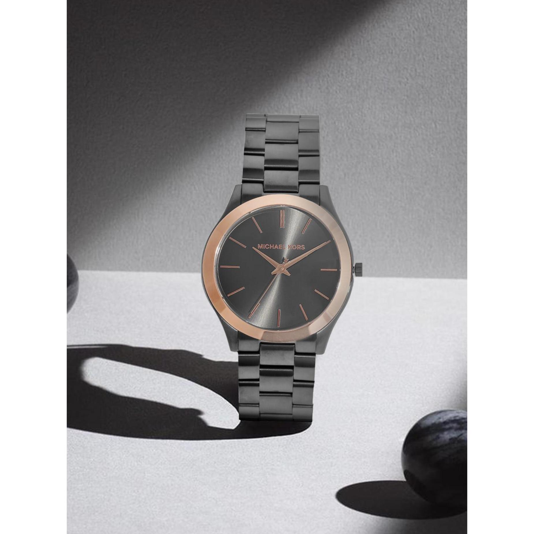 Michael Kors MK8576 women’s watch with gunmetal sunray dial, rose gold-tone bezel accents and gunmetal stainless steel bracelet displayed in shadowed setting.