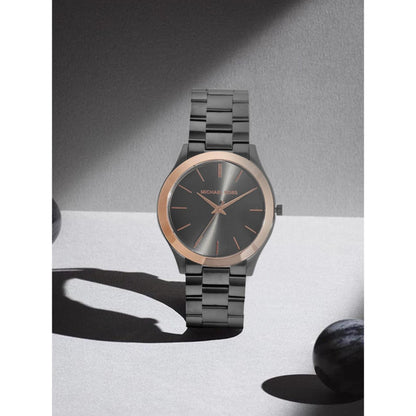 Michael Kors MK8576 women’s watch with gunmetal sunray dial, rose gold-tone bezel accents and gunmetal stainless steel bracelet displayed in shadowed setting.