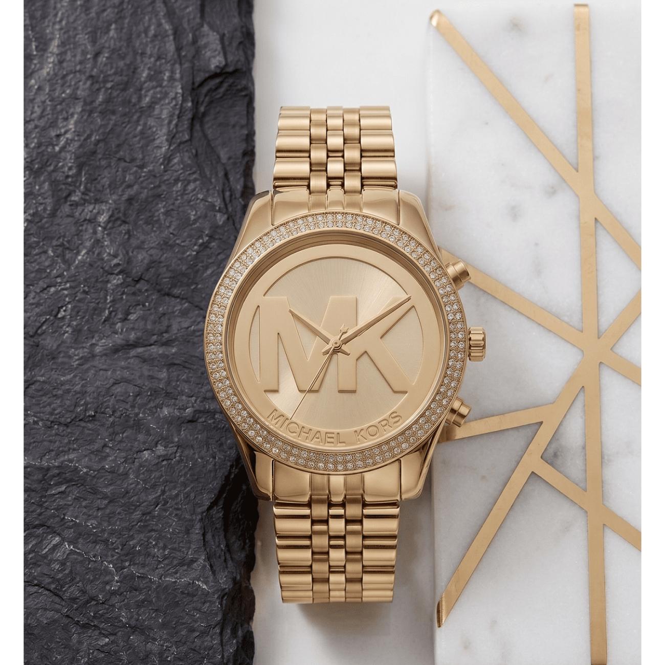 Michael Kors Parker MK5784 women’s gold-tone fashion watch with crystal-set bezel and oversized MK logo dial displayed in an elegant lifestyle setting.
