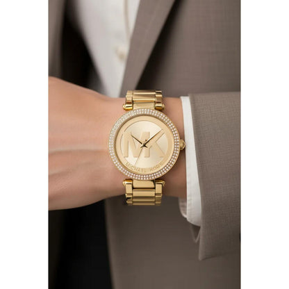 Michael Kors Parker MK5784 women’s gold-tone fashion watch with crystal-set bezel and oversized MK logo dial worn on the wrist with formal attire.