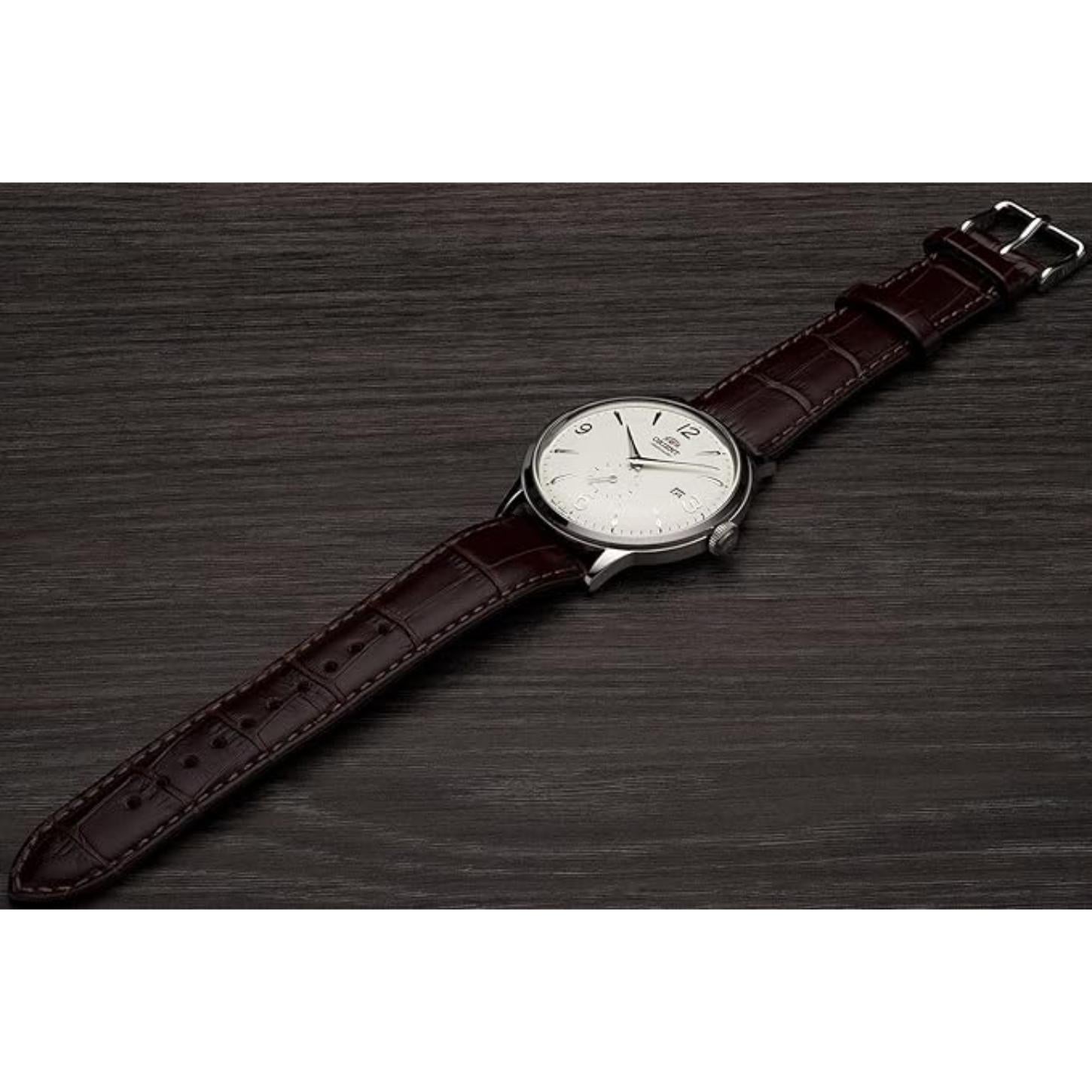 Orient Bambino Small Seconds RA-AP0002S10B automatic dress watch with white dial and brown crocodile-pattern leather strap displayed on a dark wooden surface.