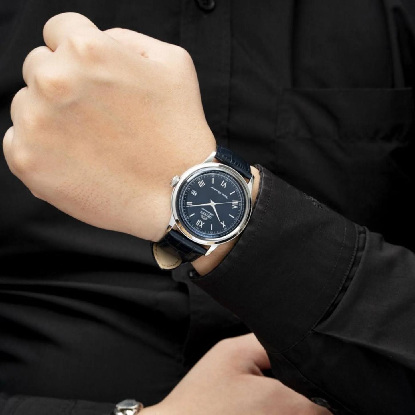 Orient RA-AC0024L30B automatic dress watch with blue sunburst dial and blue leather strap worn on the wrist with a formal black outfit.