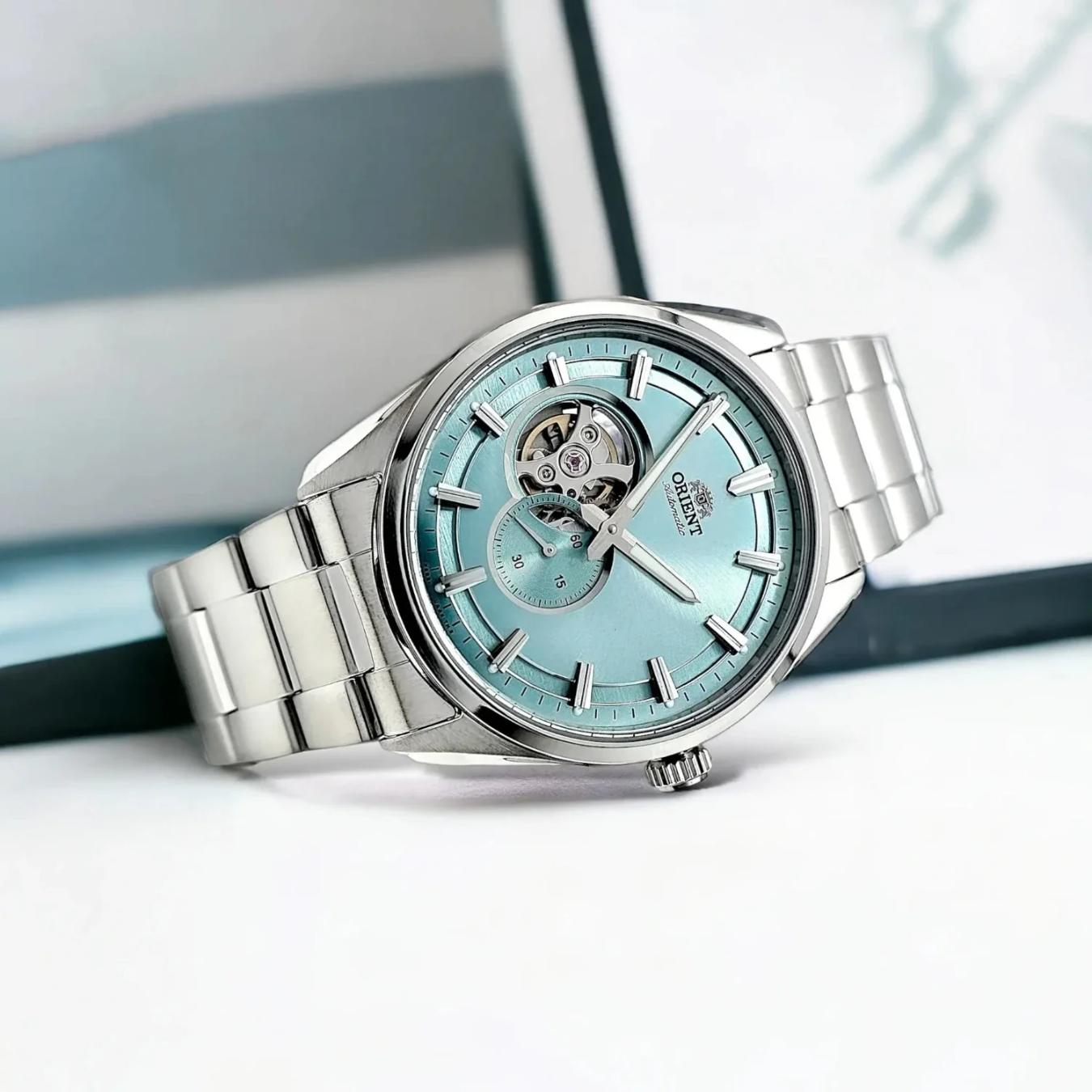 Orient RA-AR0009L automatic dress watch with light blue open-heart dial and stainless steel bracelet displayed in a bright lifestyle setting.