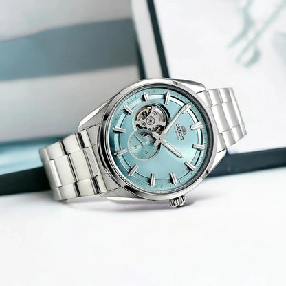 Orient RA-AR0009L automatic dress watch with light blue open-heart dial and stainless steel bracelet displayed in a bright lifestyle setting.