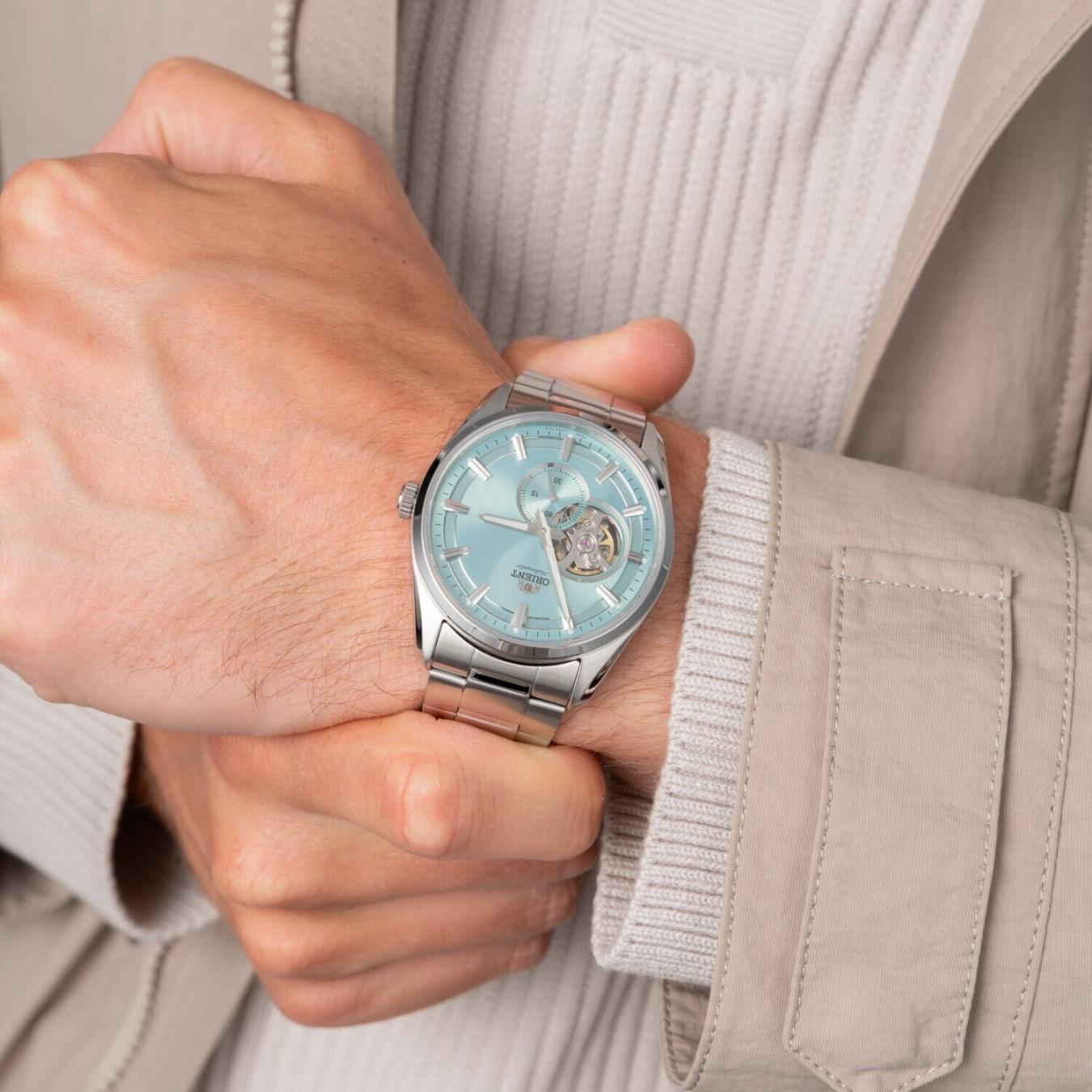 Orient RA-AR0009L automatic dress watch with light blue open-heart dial and stainless steel bracelet worn on the wrist with a light casual outfit.