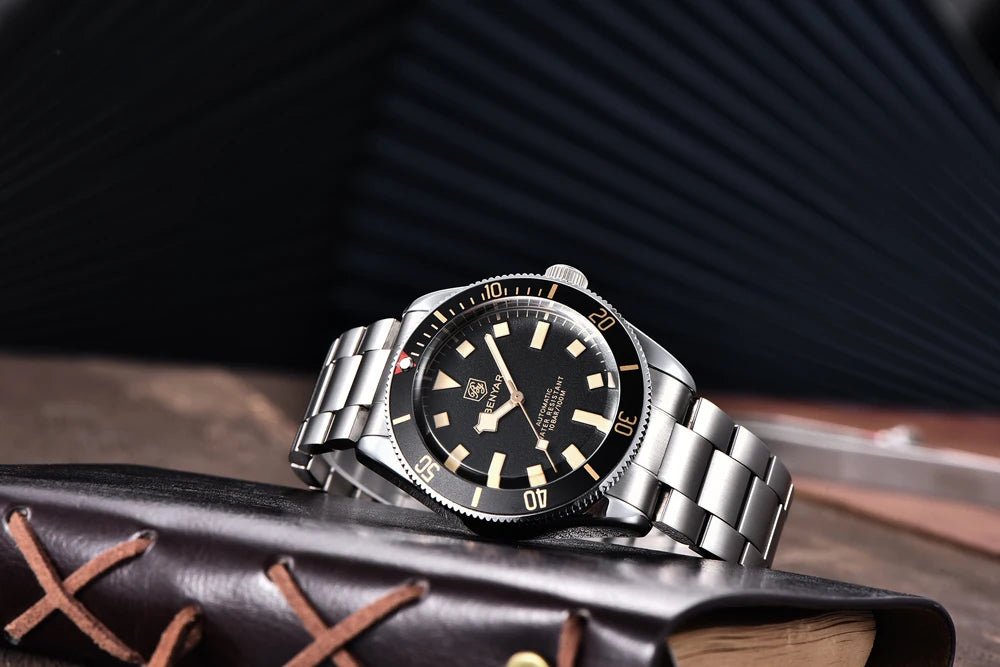 Reloj Benyar BB58 BY-5179M automático, brazalete acero y esfera negra con bisel giratorio, presentado sobre libro de cuero.